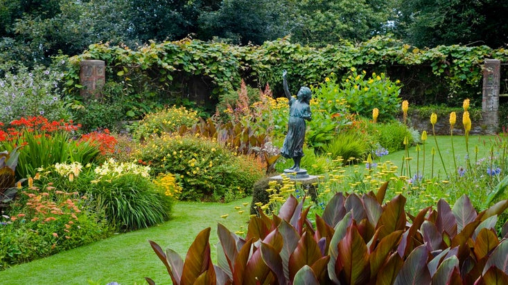 Herbaceous borders and a bronze statue, called First Flight, by Albert Bruce Joy in the Statue Garden at Overbeck's in Devon